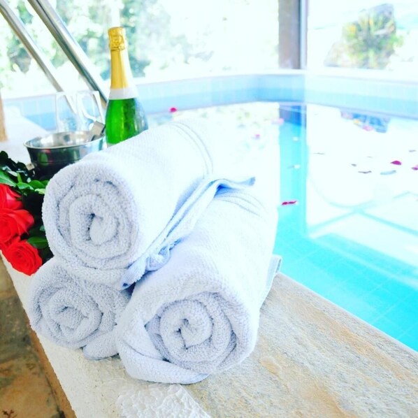 A poolside area with a stone ledge, a bottle of champagne, and rolled towels.