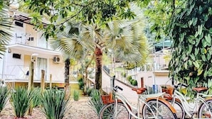 Una bicicleta estacionada bajo un árbol en un patio con edificios al fondo.