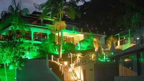Un edificio de varios pisos con una escalera que conduce a los niveles superiores, rodeado de exuberante vegetación y palmeras.