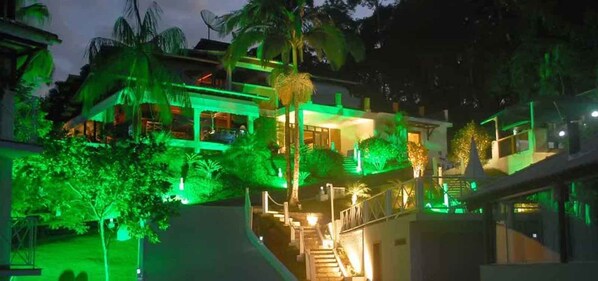 A multi-story building with a staircase leading to the upper levels, surrounded by lush greenery and palm trees.