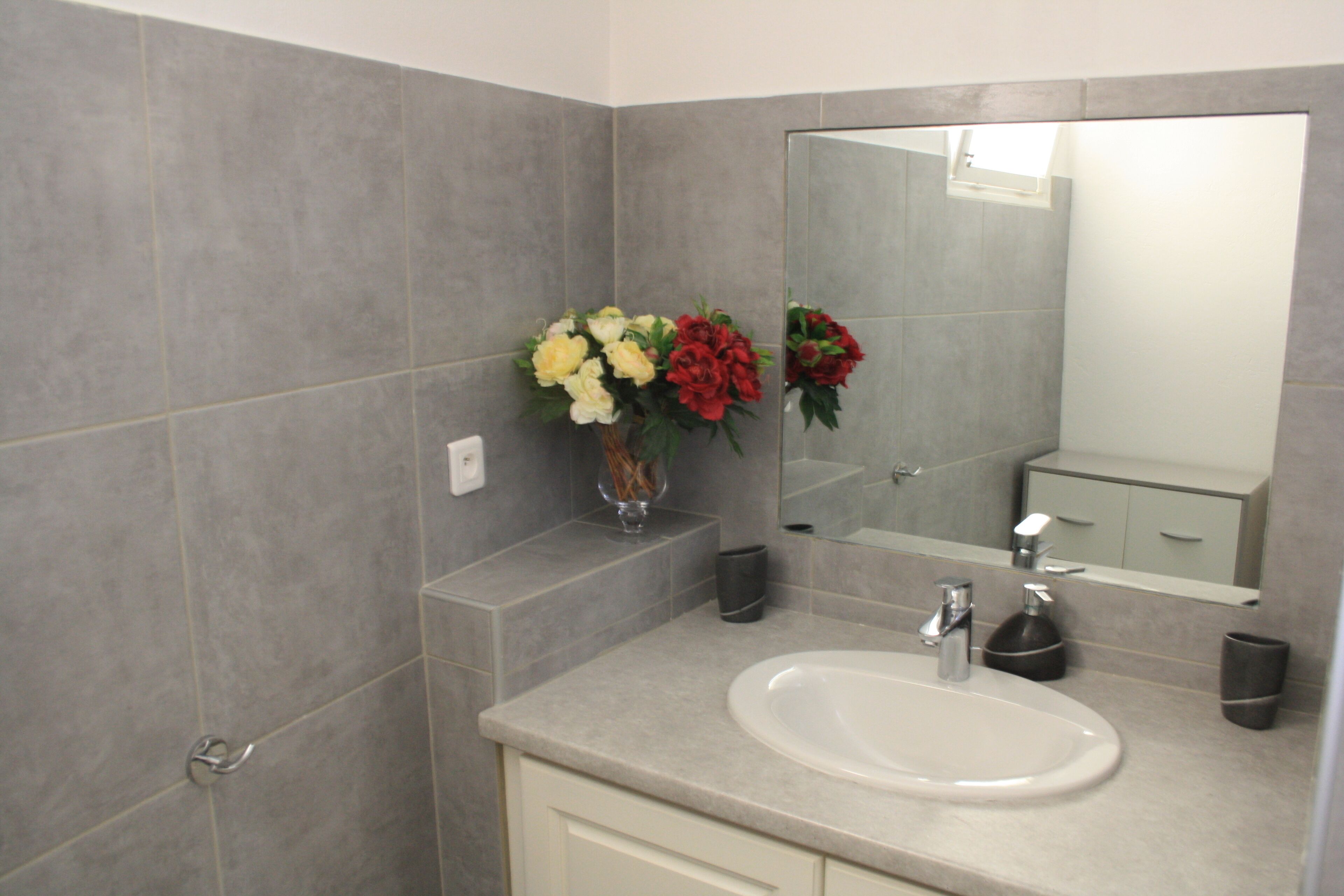 Ein Badezimmer mit Waschbecken, Spiegel und einer Blumenvase.