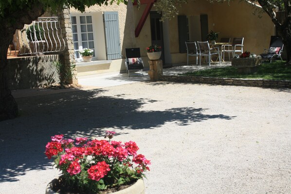 A courtyard with a seating area, a planter with red flowers, and a building with a stone facade and blue shutters.