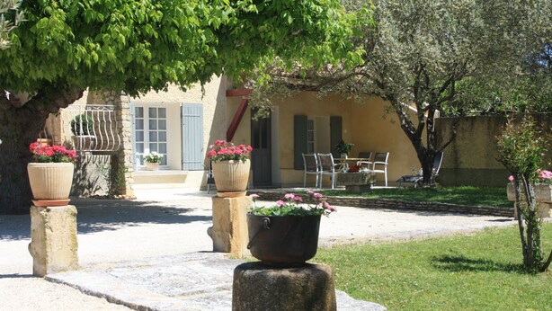Une cour avec des jardinières en pierre, une table avec des chaises et un bâtiment doté de volets.