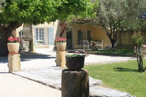 A courtyard with stone planters, a table with chairs, and a building with shutters.