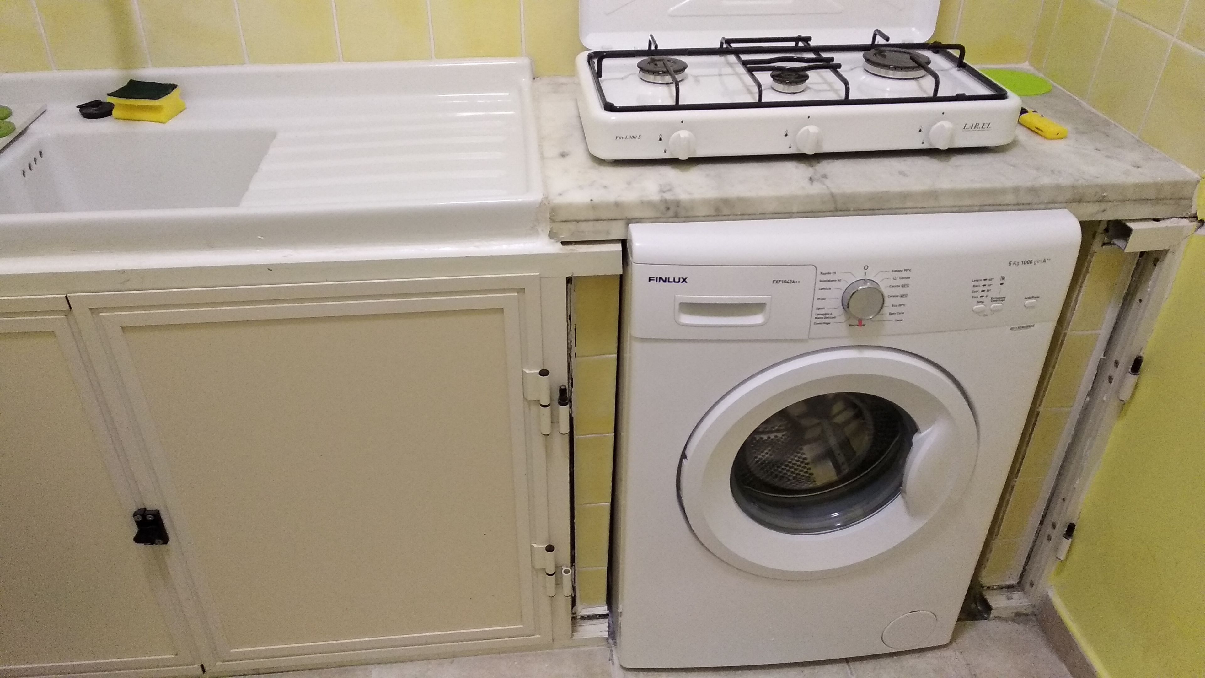 A compact kitchen with a gas stove, a washing machine, and a sink.