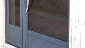 A sliding glass door with a metal handle, leading to a room with a tiled floor and a stone wall. - B&B Rossini (Augusta)