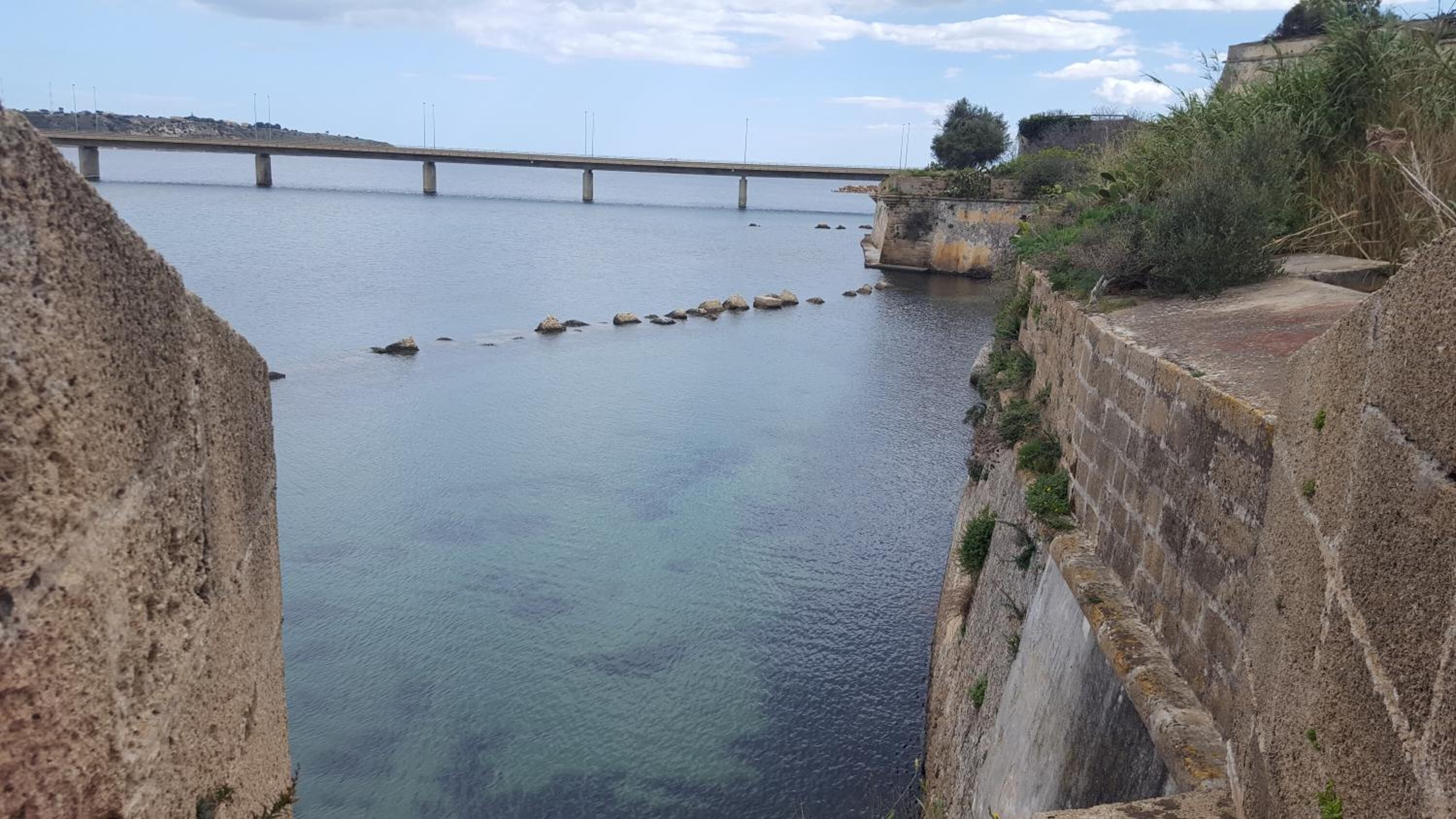 Eine Brücke über einem ruhigen Fluss, mit einer Steinmauer auf einer Seite und Vegetation auf der anderen.