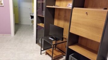 Una stanza con una televisione su un supporto nero, mensole di legno e un pavimento piastrellato.