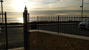 A parking area with a stone wall and metal fence, a car, and a sunset in the background. - B&B Rossini (Augusta)