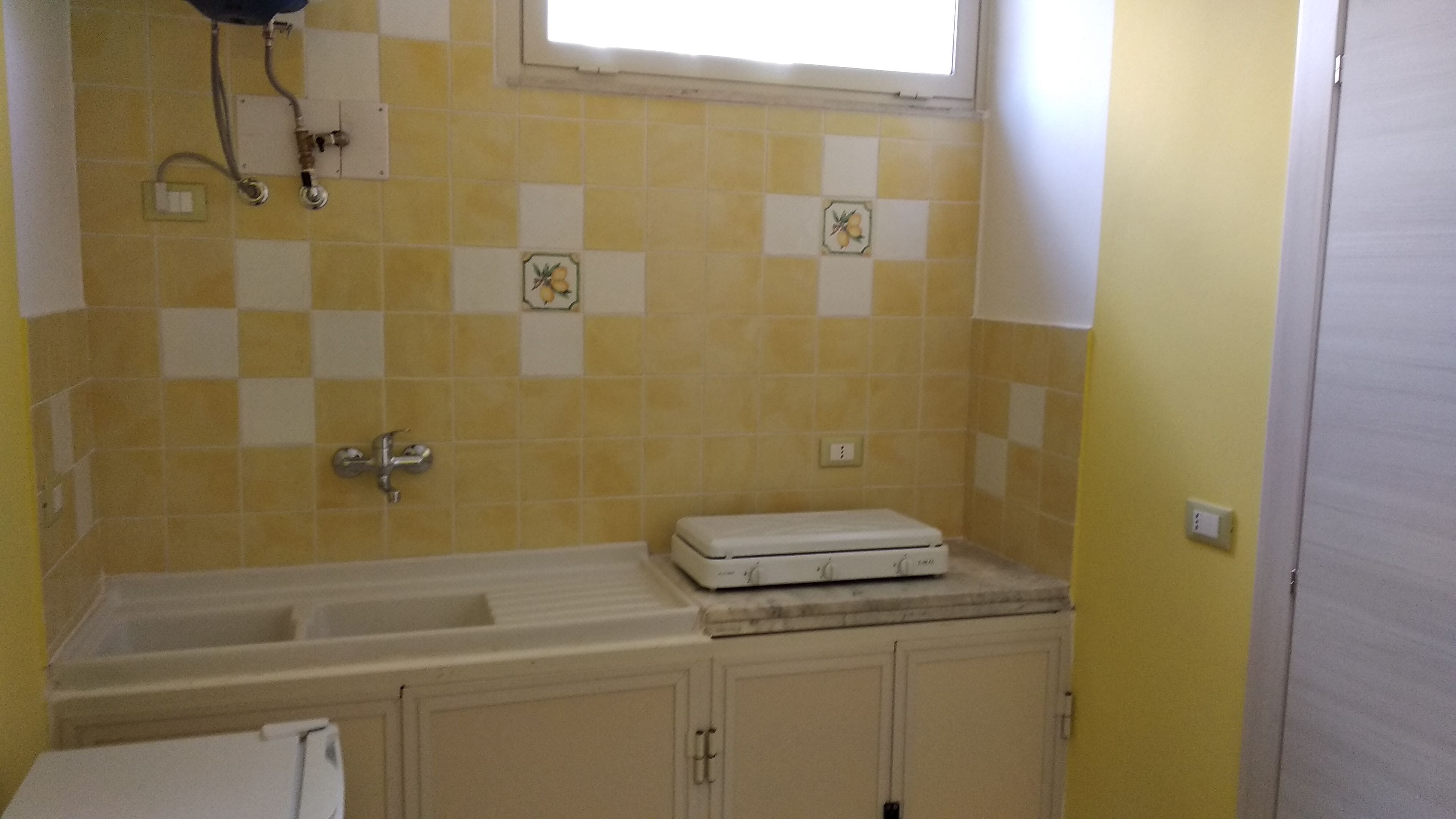 Un baño con baldosas blancas y amarillas a cuadros, una bañera blanca, una toalla blanca y una ventana sobre el lavabo.