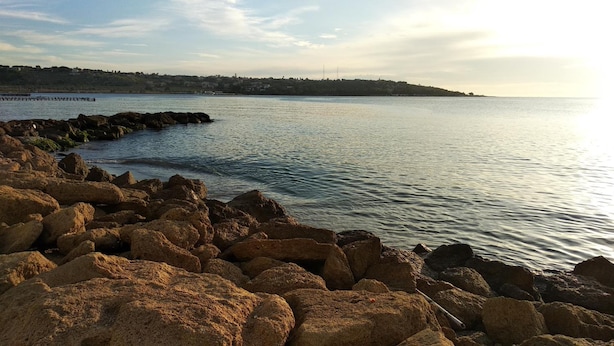 A rocky shoreline with calm water and a distant view of a town. - B&B Rossini (Augusta)