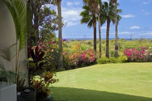 A well-maintained garden with palm trees, flowering plants, and a clear view of the ocean. - Stunning ocean sunsets @ Wailea Beaches, foodie kitchen! Sept deep discounts! (Kihei)