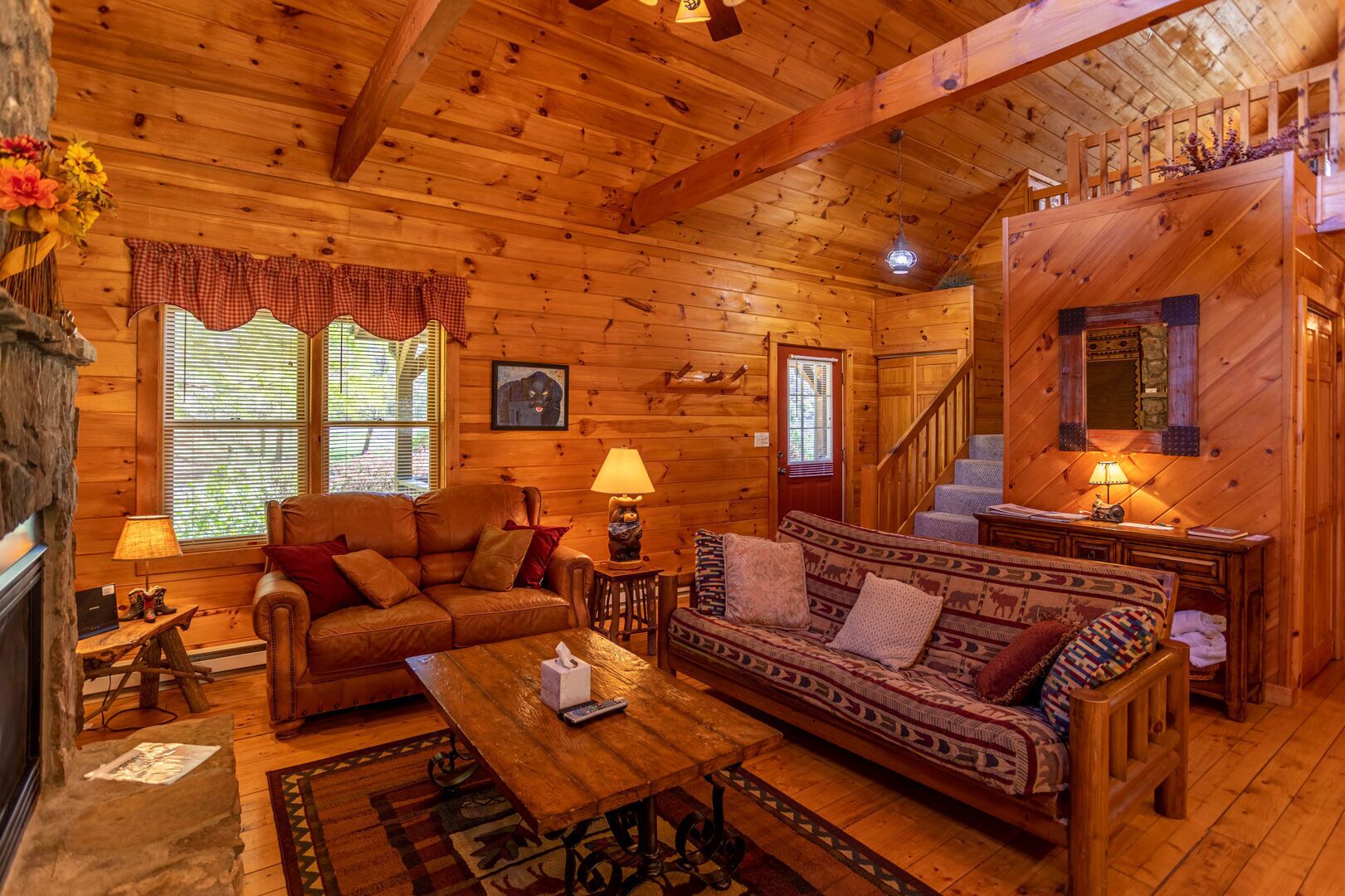 L’intérieur chaleureux d’un chalet en bois comprend une cheminée, un canapé en cuir, une table à manger en bois et un escalier menant à un étage supérieur.