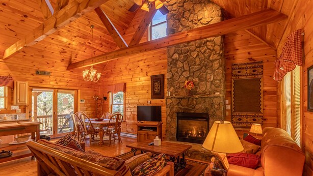 A cozy cabin interior with a stone fireplace, wooden furniture, and a dining area. - Baird's Creek Cabin  Cozy Cabin, Close to Golf, Creekside (Vilas)