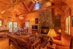Cozy cabin-style interior with a stone fireplace, comfortable seating area, and dining table for four.