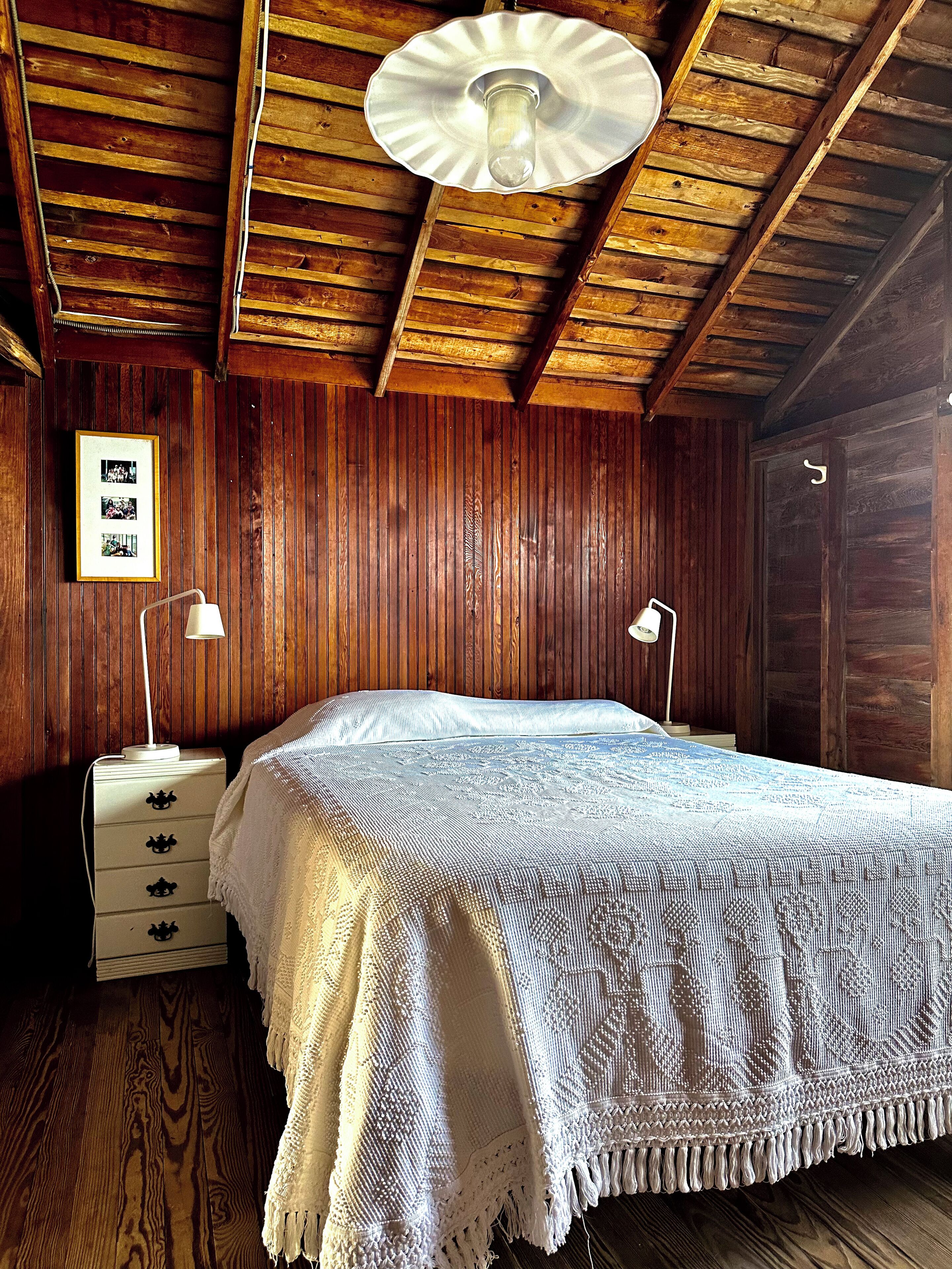 A wooden-paneled room with a bed, two bedside lamps, a dresser, and framed pictures on the wall.