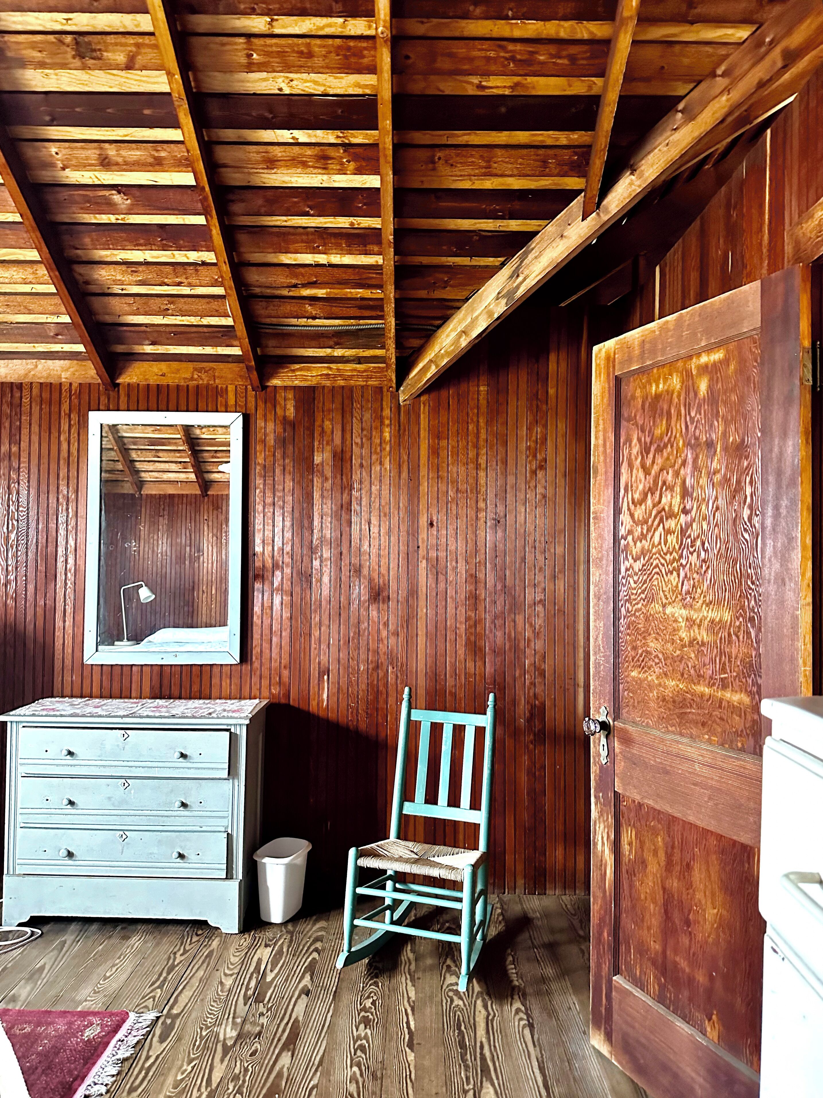 Une pièce en bois, avec une commode, une chaise et une grande porte.