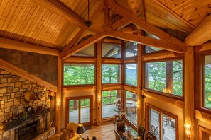 Un chalet spacieux doté d’une cheminée en pierre, de grandes fenêtres et d’une terrasse en bois.