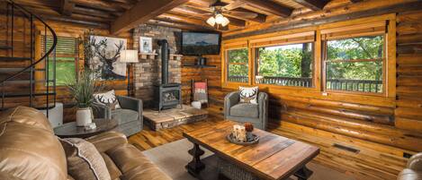 A log cabin interior with a fireplace, a sofa, a coffee table, and a television.
