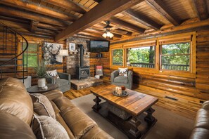 A log cabin interior with a fireplace, a sofa, a coffee table, and a television. - Riverside Retreat | Private Riverfront, Hot Tub, Game Room & Fire Pit (Boone)
