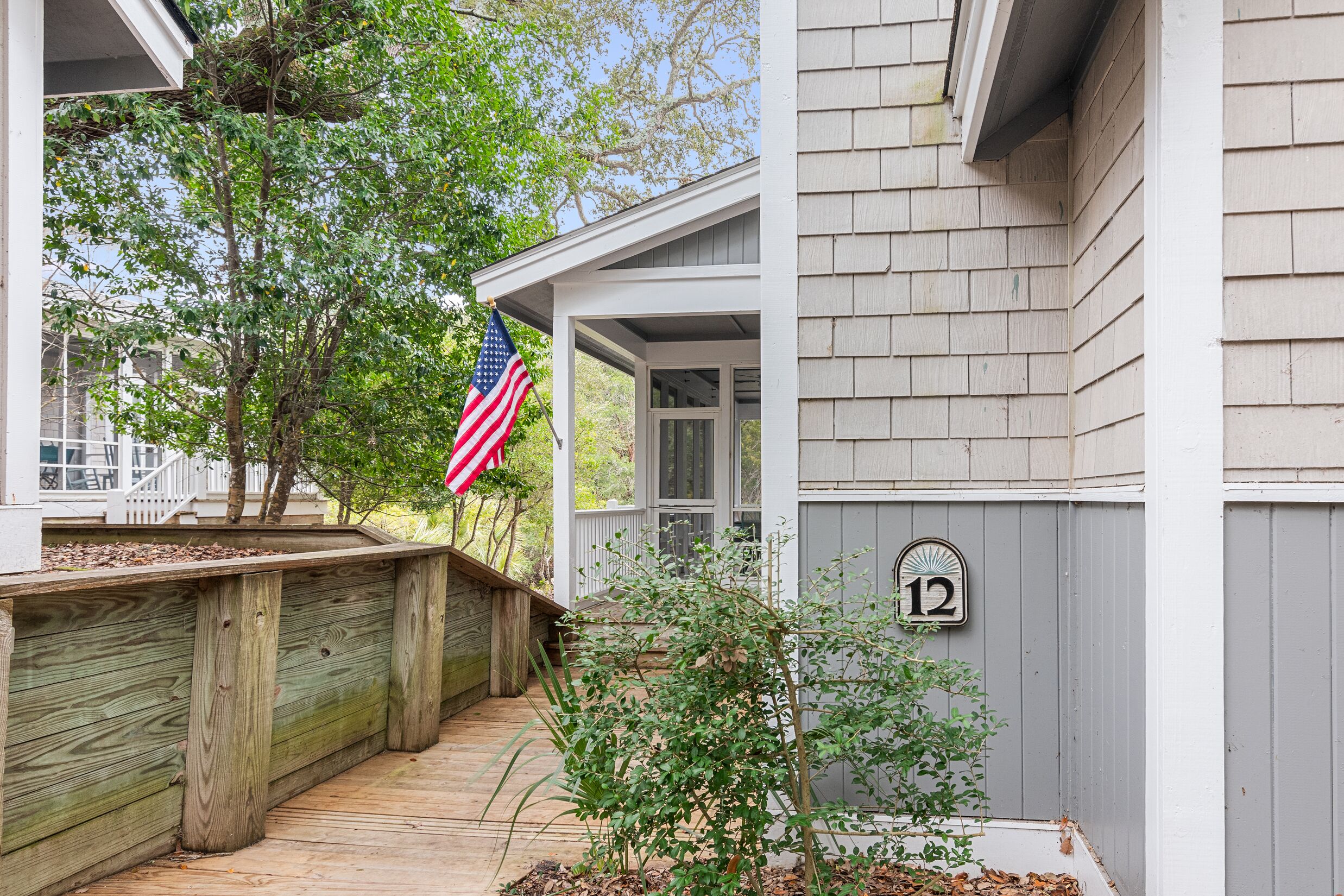 A wooden deck leading to a house with a number 12 sign, a small tree, and an American flag.