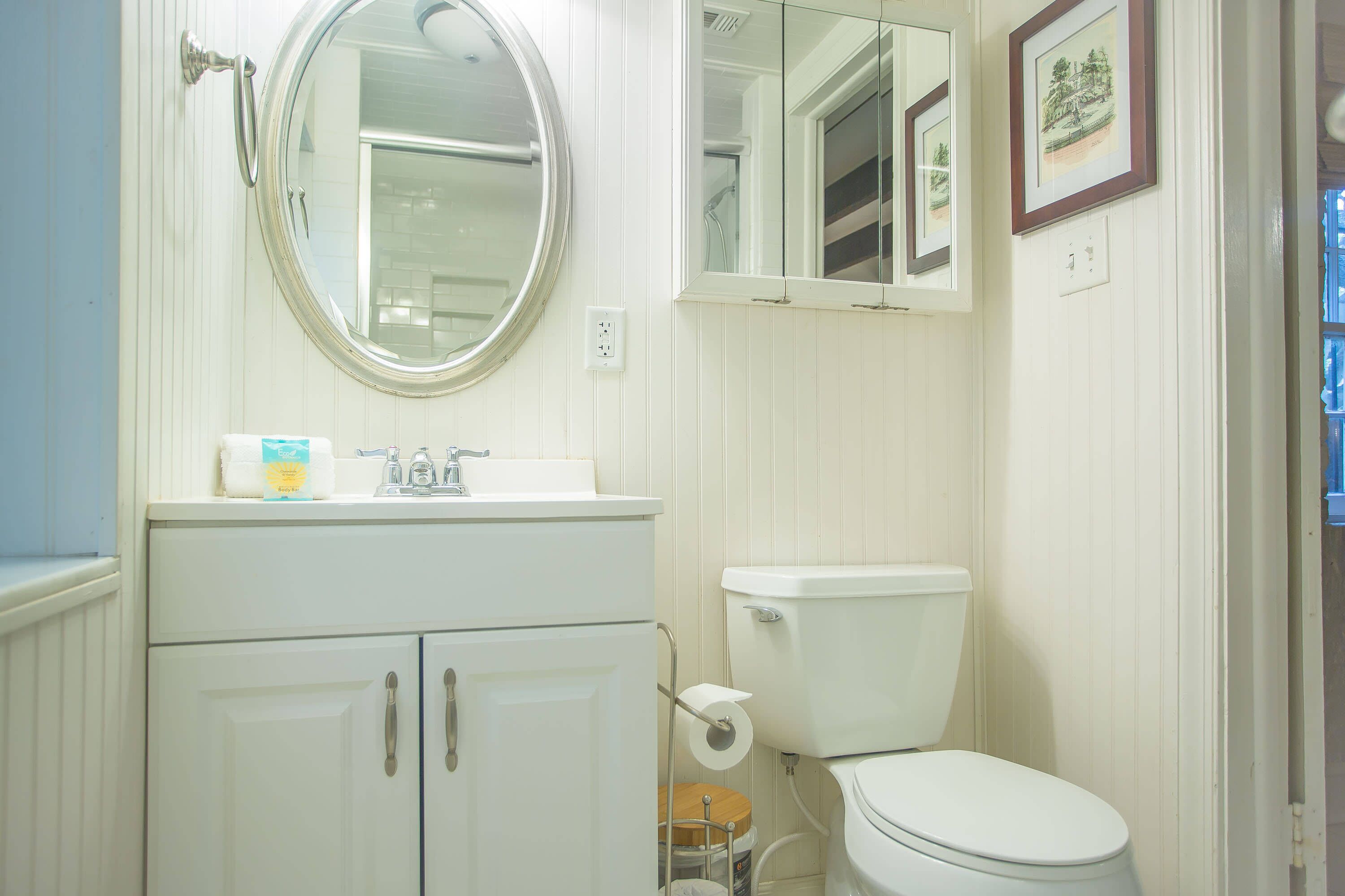 A bathroom with a white sink, mirror, toilet, and cabinets.