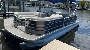 A pontoon boat docked at a marina with a covered seating area, a steering wheel, and a registration number visible. - Cozy Waterfront Home with private dock, and access to the intercoastal waterway. (Palm Harbor)