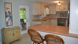 A kitchen with white cabinets, a large island, and a dining area with wicker chairs. - Cozy Waterfront Home with private dock, and access to the intercoastal waterway. (Palm Harbor)