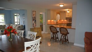 A spacious living area with a wooden dining table, white chairs, and a kitchen area with white cabinets and a wooden island. - Cozy Waterfront Home with private dock, and access to the intercoastal waterway. (Palm Harbor)