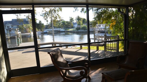 A room with large windows overlooking a body of water, wooden flooring, and two wicker chairs. - Cozy Waterfront Home with private dock, and access to the intercoastal waterway. (Palm Harbor)