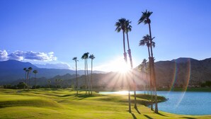 Un parcours de golf bordé de palmiers, avec un lac et des montagnes en arrière-plan.