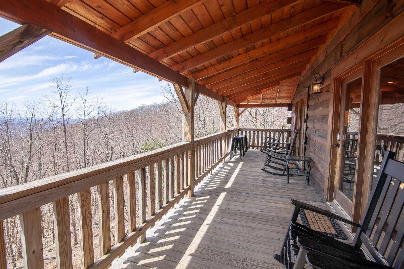 A wooden deck with a railing, benches, and a view of the surrounding forest.