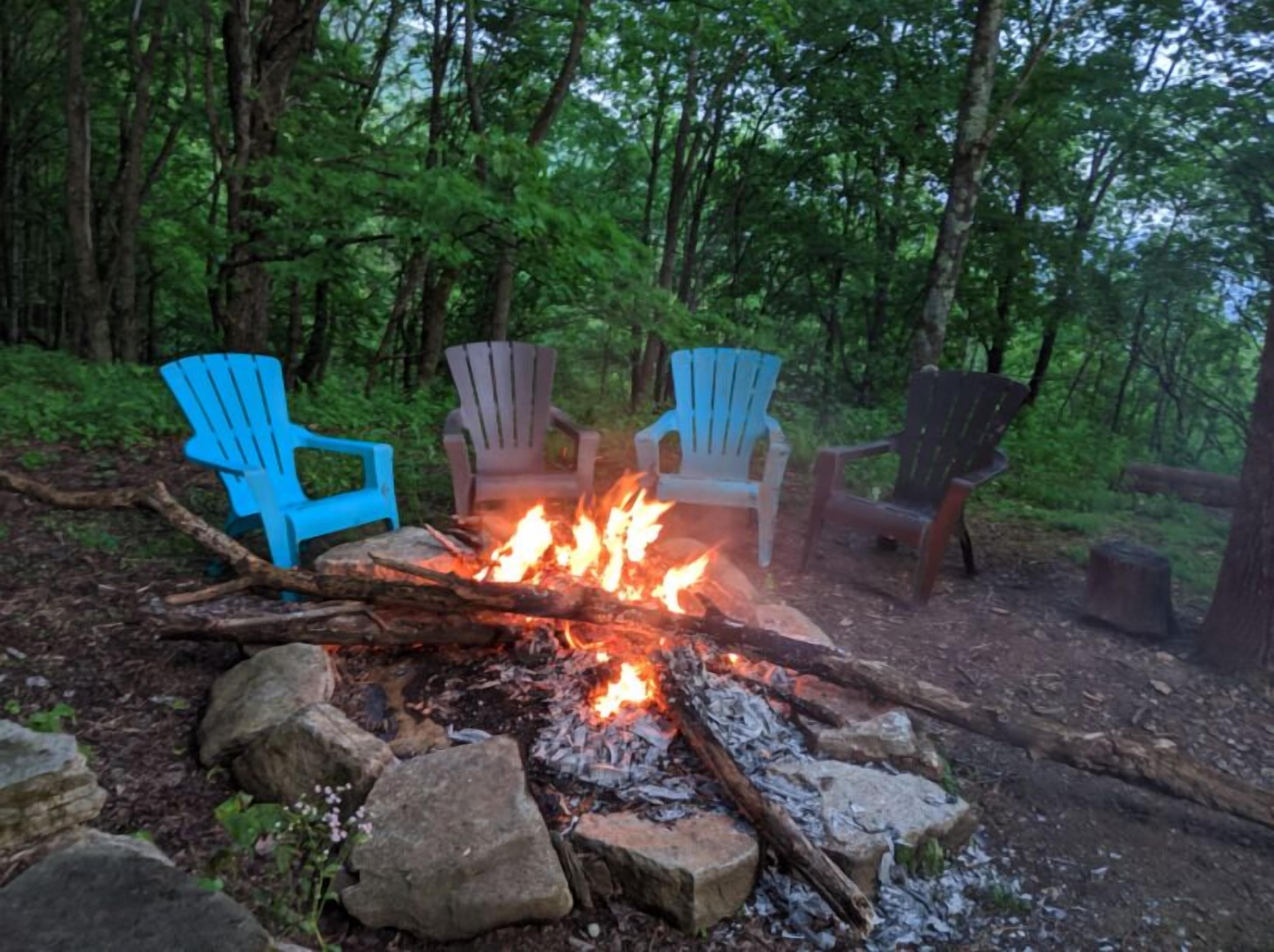 Een kampvuur met vier Adirondack stoelen eromheen, gelegen in een bebost gebied.