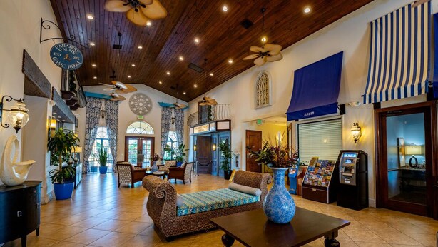 A spacious lobby with a high ceiling, wooden beams, and a mix of seating areas including a sofa and chairs. - Beautiful Town Home in Gated Community with Extensive Facilities (Kissimmee)