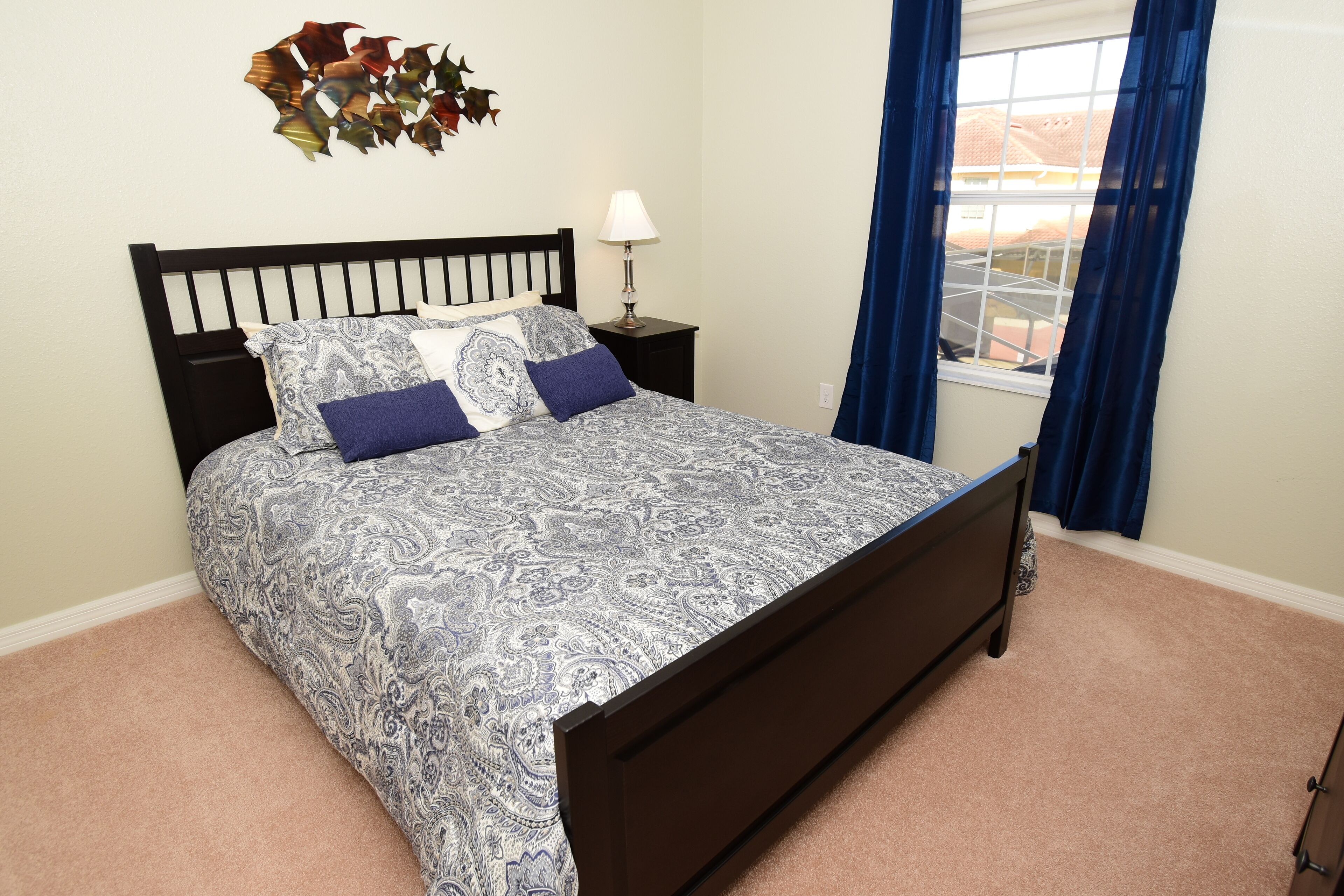 A bedroom with a bed, a nightstand, a lamp, and a window with curtains.