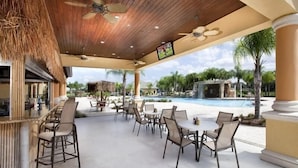 An outdoor seating area with tables and chairs, a pool, and a thatched roof structure. - Beautiful Town Home in Gated Community with Extensive Facilities (Kissimmee)