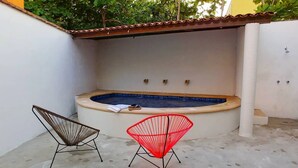 Un área pequeña para jacuzzi al aire libre con dos sillas, una marrón y otra roja, y piso de baldosas.