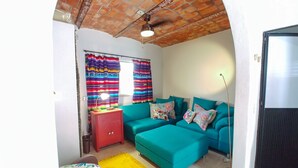 Una sala de estar con un sofá color turquesa, cortinas coloridas, un armario rojo y una alfombra amarilla.