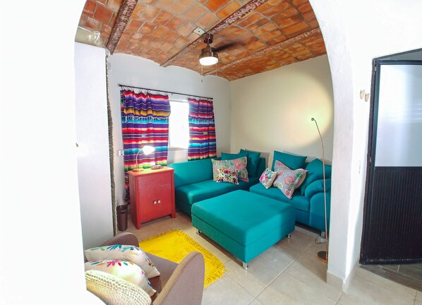 A living room with a teal sofa, colorful curtains, a red cabinet, and a yellow rug.