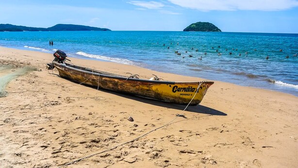 Una playa con un bote llamado 'Carnelita' y una pequeña isla al fondo.