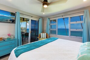 A bedroom with a large bed, a ceiling fan, and a view of the ocean through large windows.