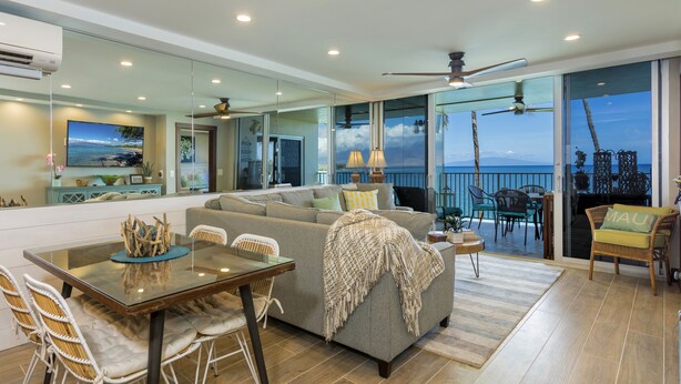 Uma sala de estar moderna com uma mesa de jantar de vidro, um sofá com manta e vista para o oceano através de grandes janelas.