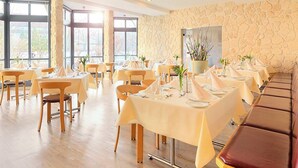 A restaurant with multiple tables set for dining, stone walls, and large windows. - aktiv Sporthotel (Pirna)