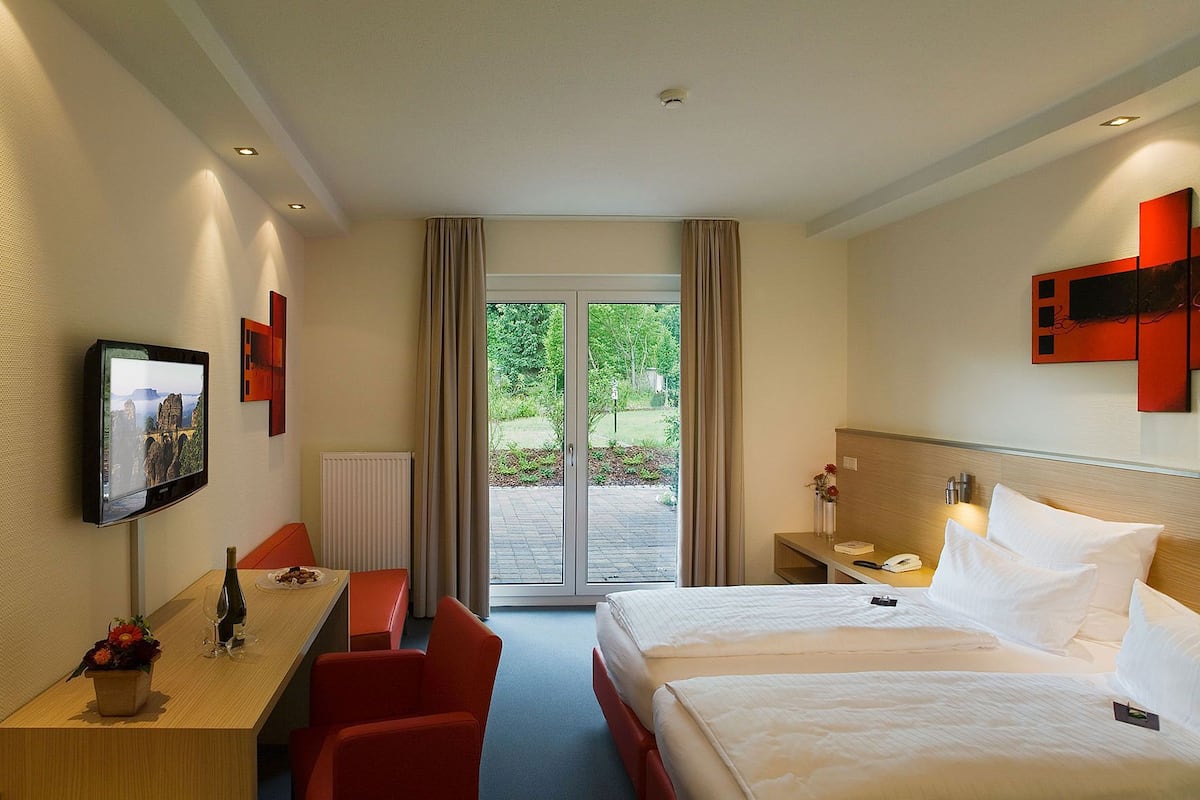A hotel room with a bed, a desk, a chair, a TV, and a view of the outdoors.
