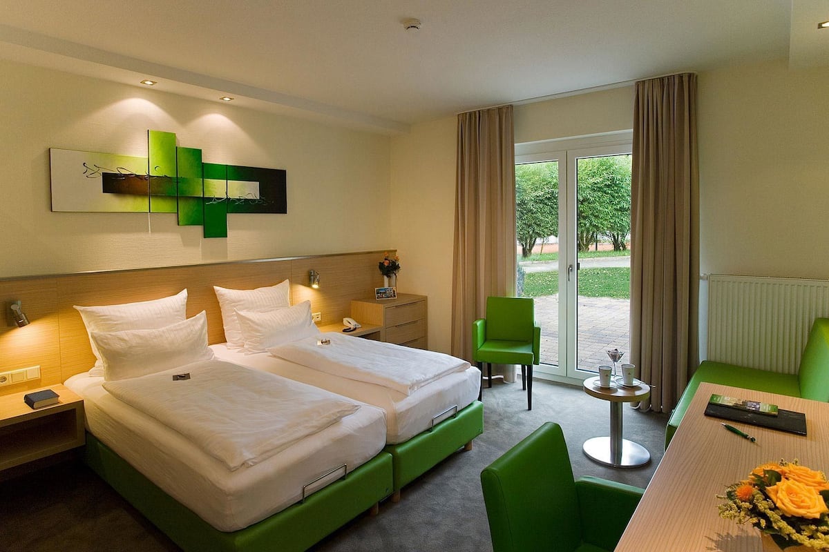 A hotel room with two beds, a desk, a chair, and a view of the outdoors.