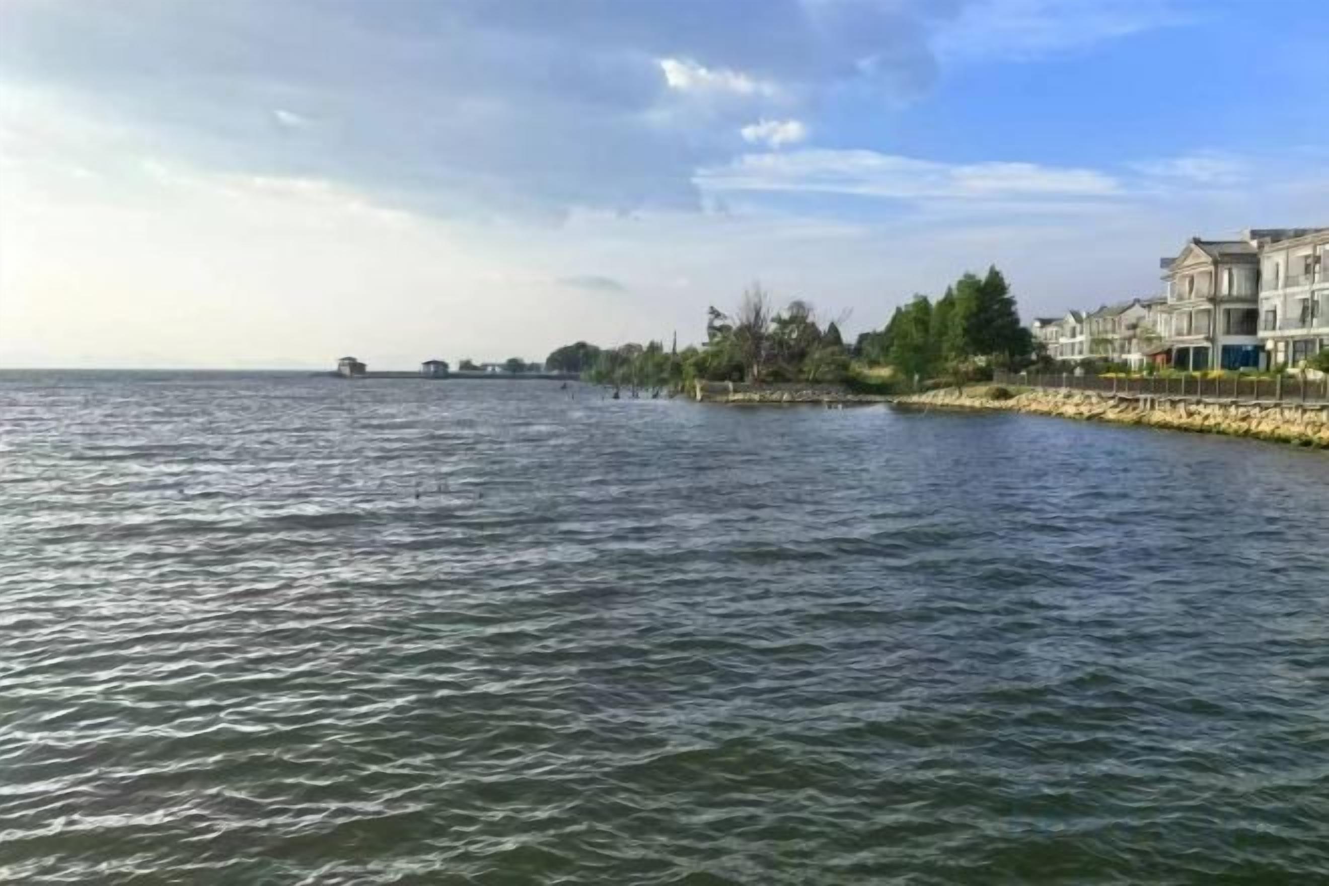 A waterfront view with a calm body of water, a stone embankment, and buildings along the shore.