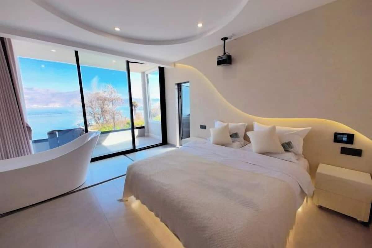 A modern bedroom with a large bed, a curved headboard, and a view of the outdoors.
