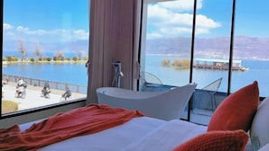 A modern hotel room with a large window, a bathtub, and a bed with pillows. - Dali Haitian Yihaijing Inn (Dali City)