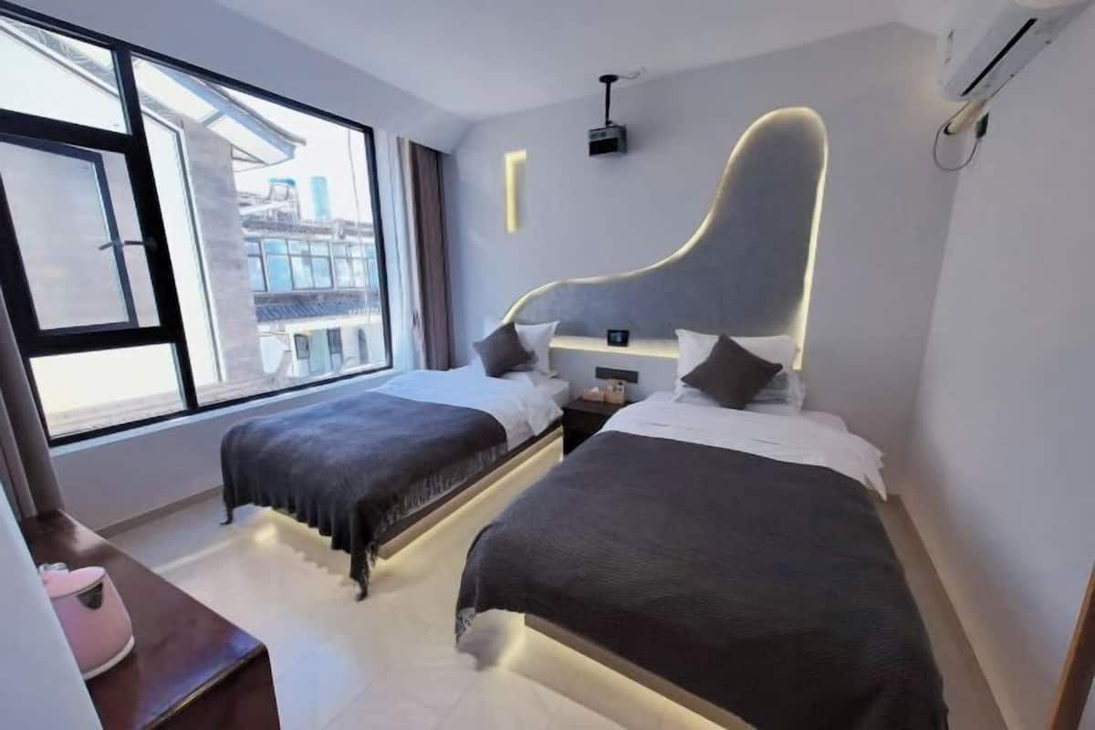 A modern hotel room with two beds, a large window, and a view of the city.