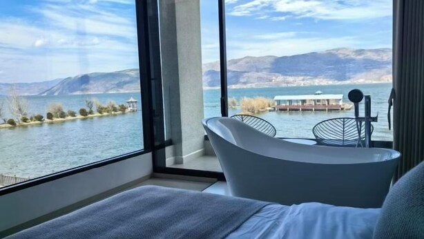 A modern room with a large window overlooking a lake and mountains, a bed, and a small table with chairs. - Dali Haitian Yihaijing Inn (Dali City)